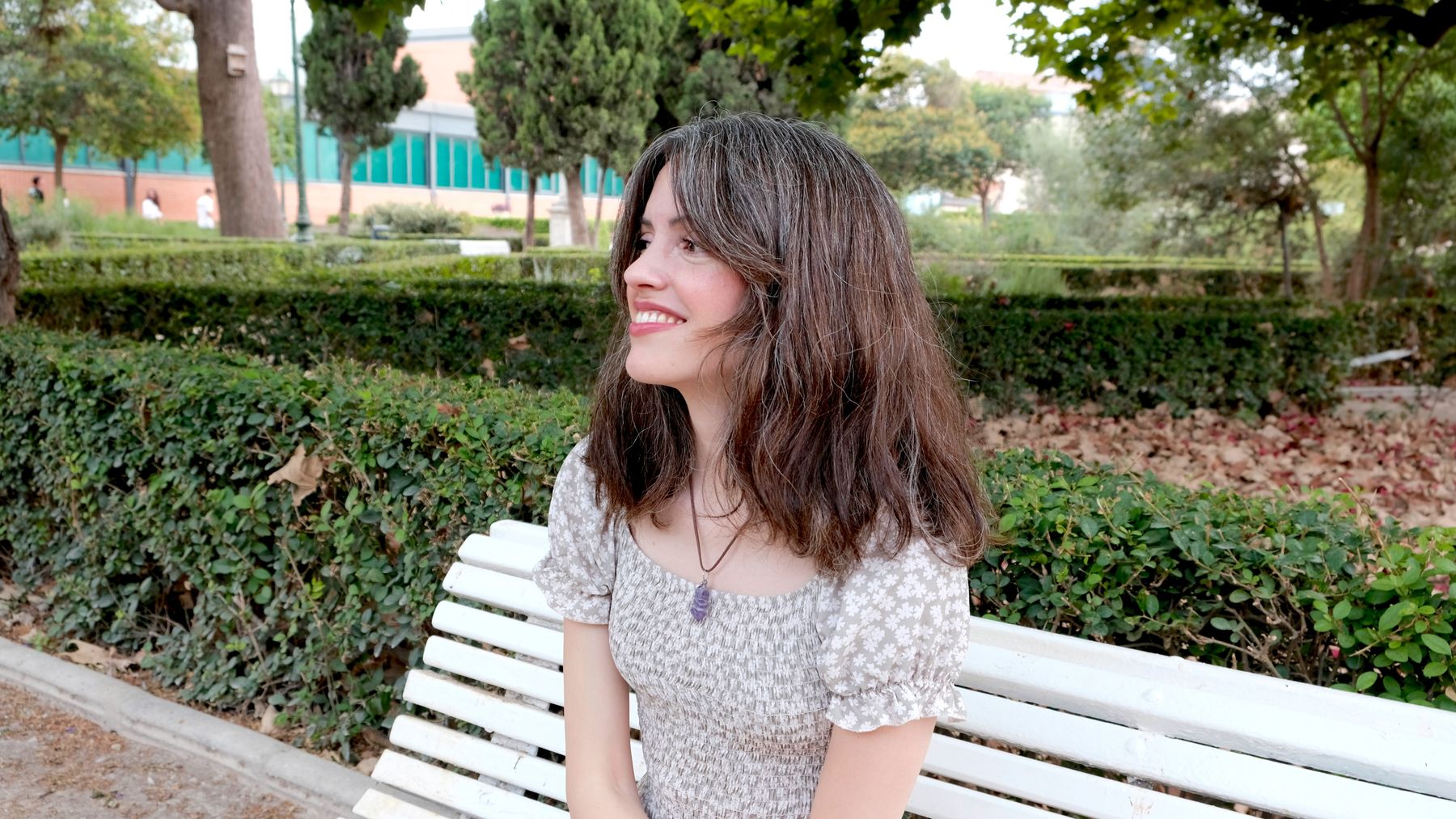 Andrea Picó sentada en un banco blanco en un parque, sonriendo